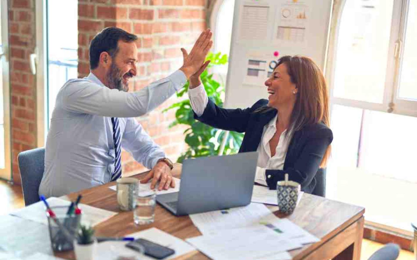 Two people at work high fiving at a desk